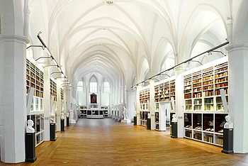 Flur einer Bibliothek mit Bücherregalen und kleinen Statuen